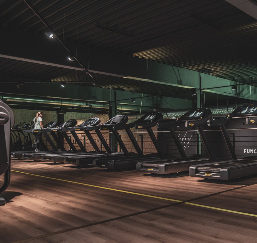 Photograph of a gym interior, a row of treadmills.